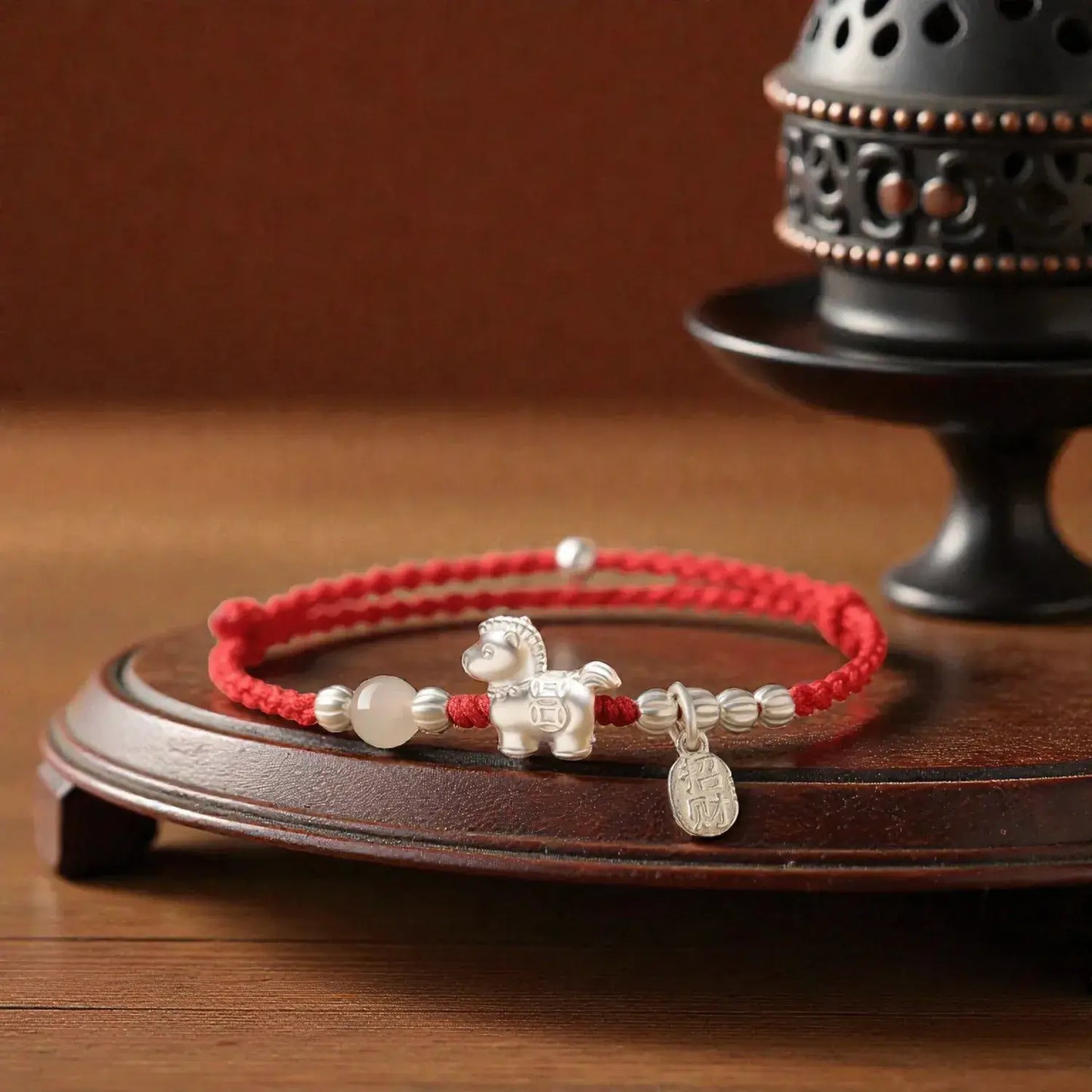 Red bracelet with silver horse charm on a wooden stand with an incense burner in the background