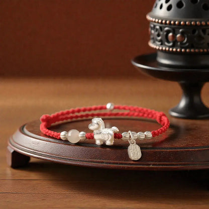 Red bracelet with silver horse charm on a wooden stand with an incense burner in the background