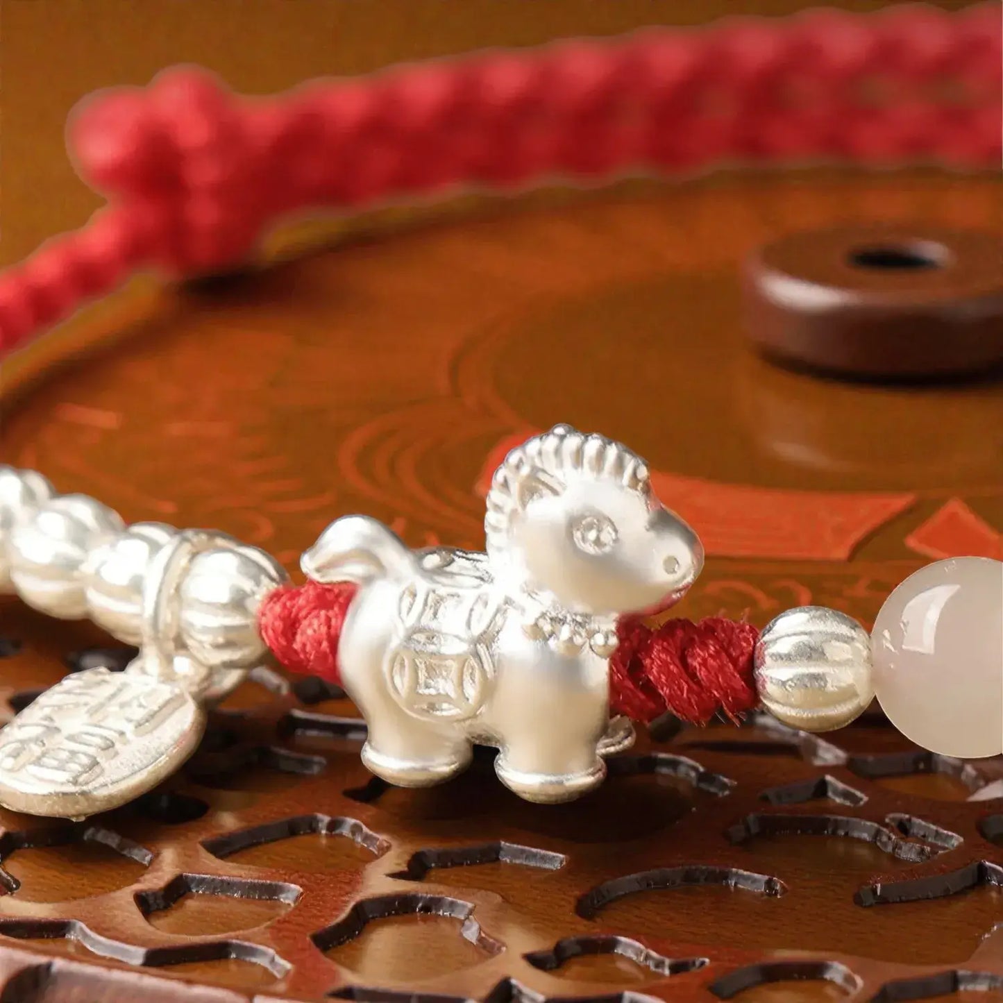 Silver dog-shaped charm on a red string with white beads on a decorative wooden surface