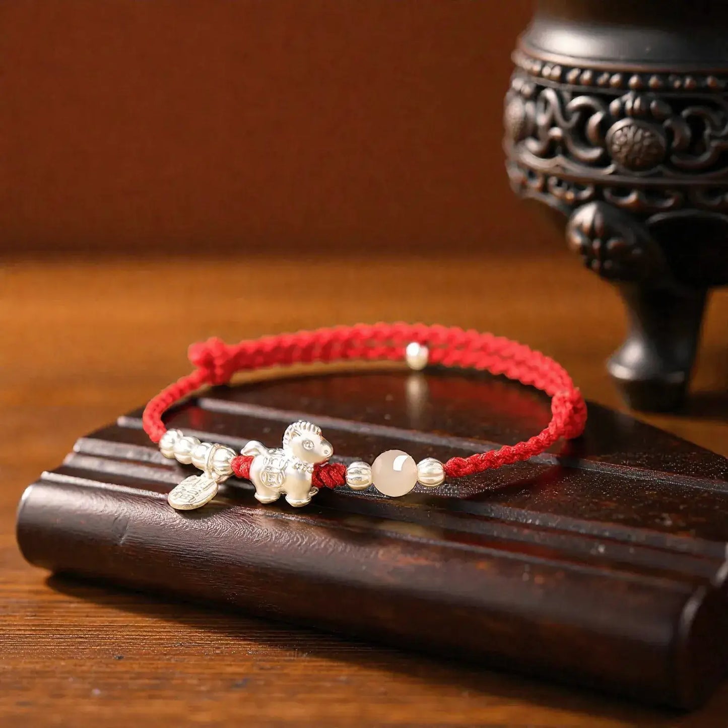 Red string bracelet with silver beads on a wooden surface