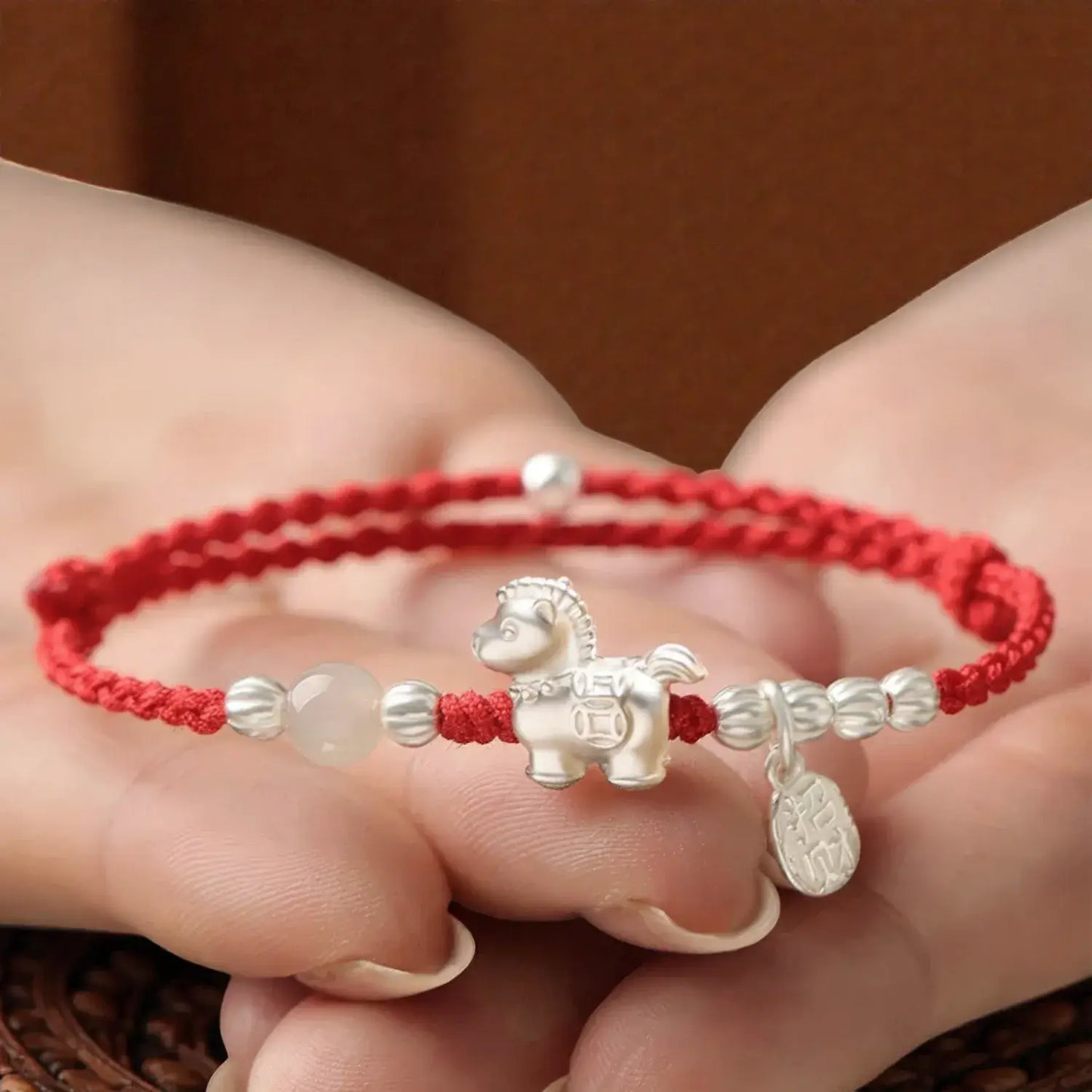Red string bracelet with a silver horse charm held in a hand against a brown background