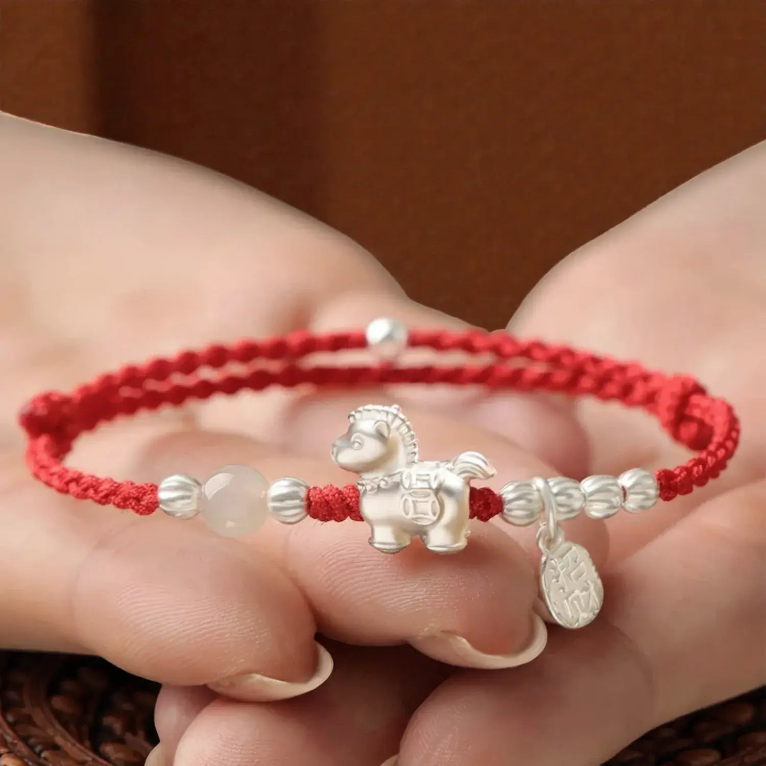 Red string bracelet with a silver horse charm held in a hand against a brown background