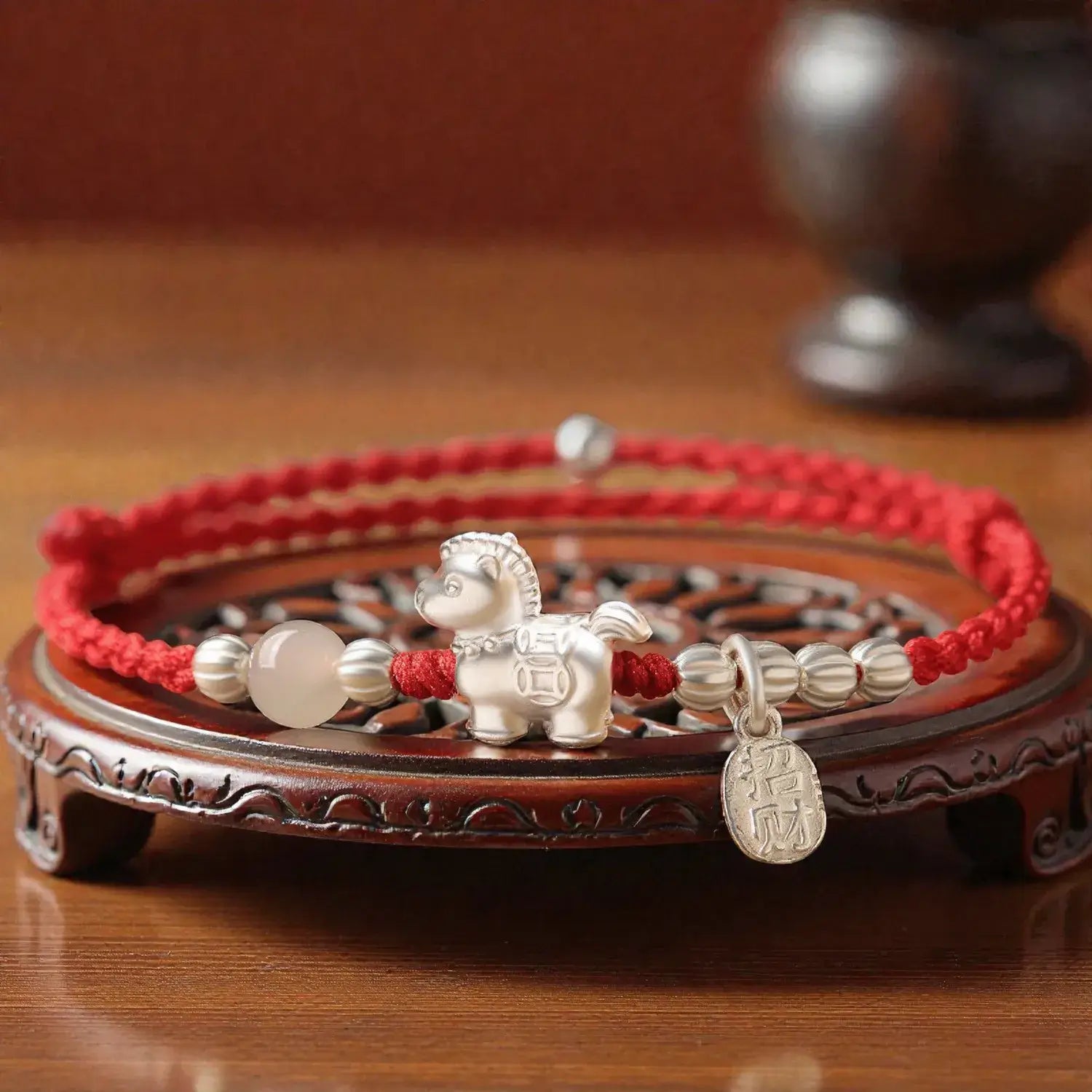 Bracelet with silver horse charm and red string on a wooden stand