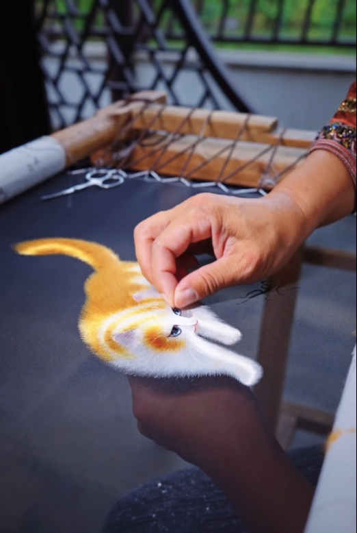 Person working on a needlepoint project with a cat design.