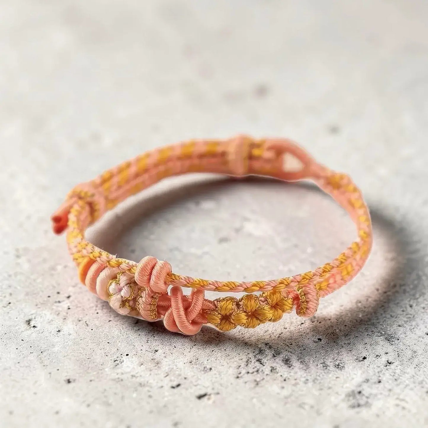 Pink and yellow braided bracelet on a textured surface