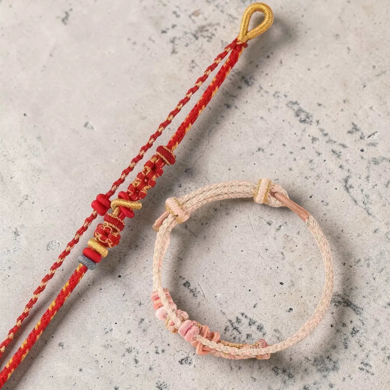 Two bracelets, one red and gold, the other pink and beige, on a textured surface.