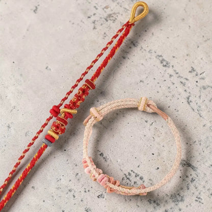 Two bracelets, one red and gold, the other pink and beige, on a textured surface.