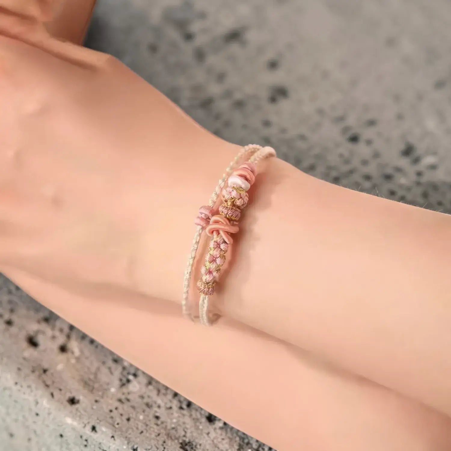 Close-up of a wrist wearing a pink beaded bracelet on a neutral background