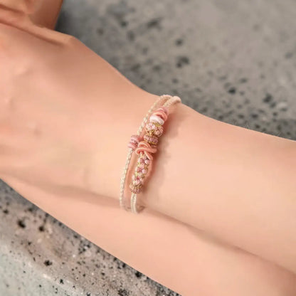 Close-up of a wrist wearing a pink beaded bracelet on a neutral background