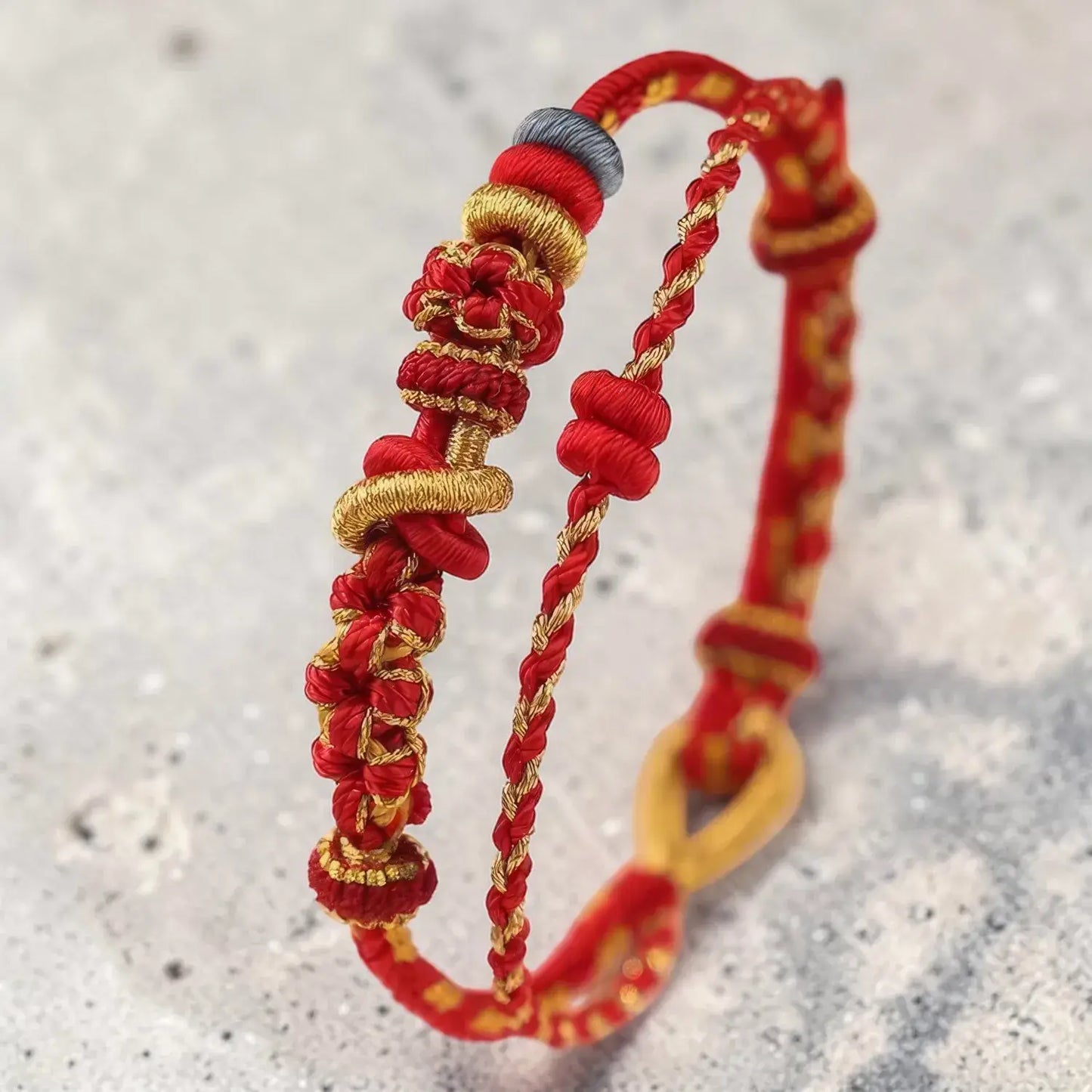 Two red and gold braided bracelets on a textured gray background