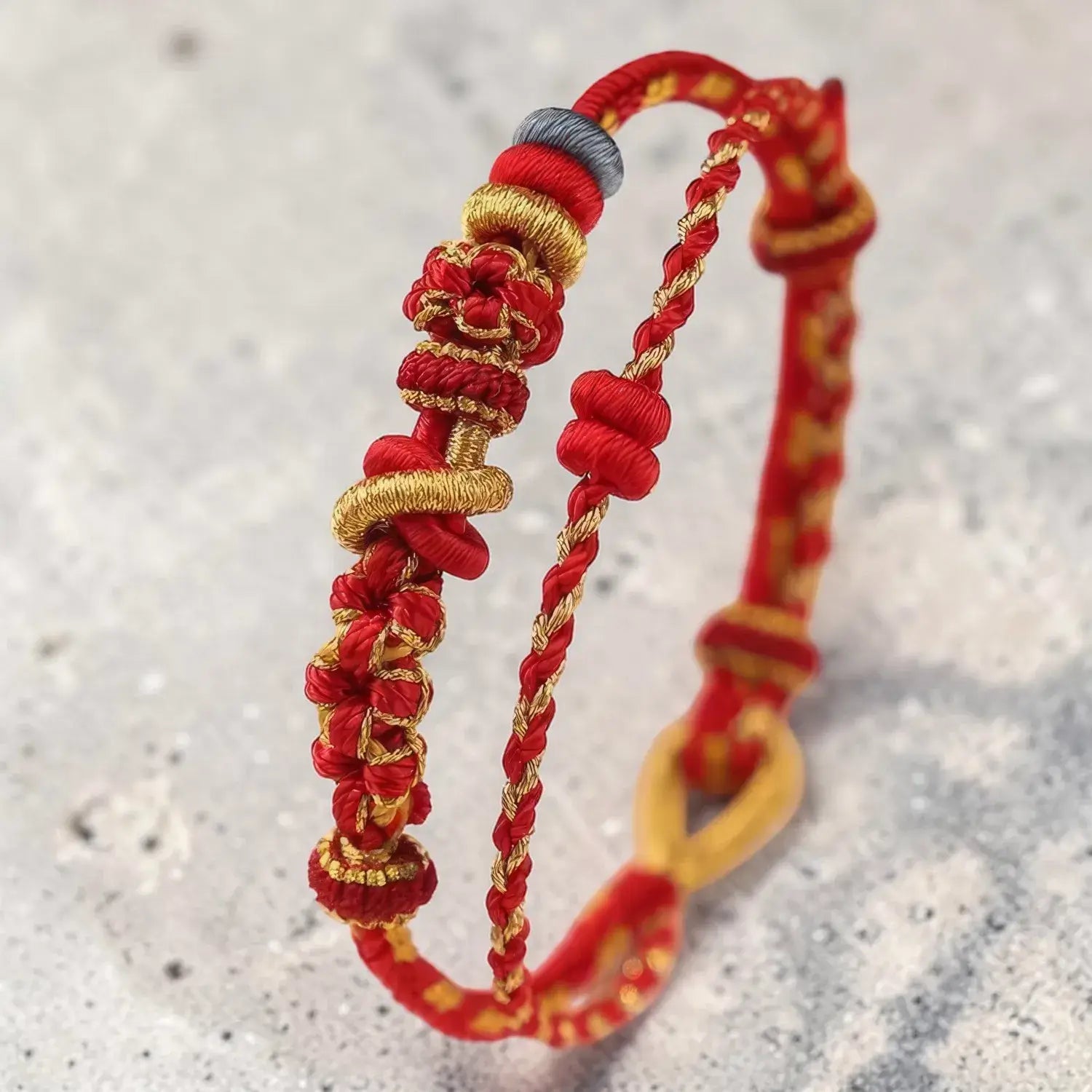 Two red and gold braided bracelets on a textured gray background