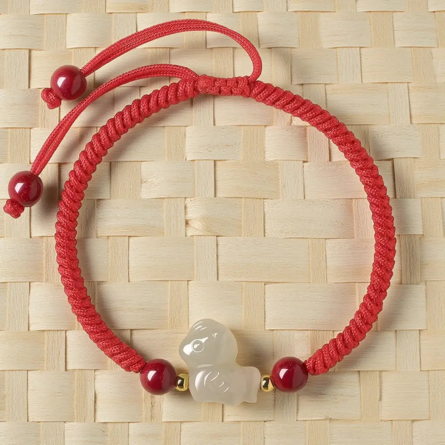 Red bracelet with a white charm on a woven beige background