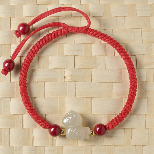 Red bracelet with a white charm on a woven beige background