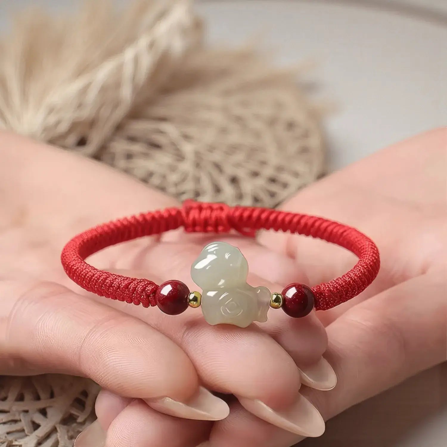 Red string bracelet with a jade charm held in a hand against a neutral background
