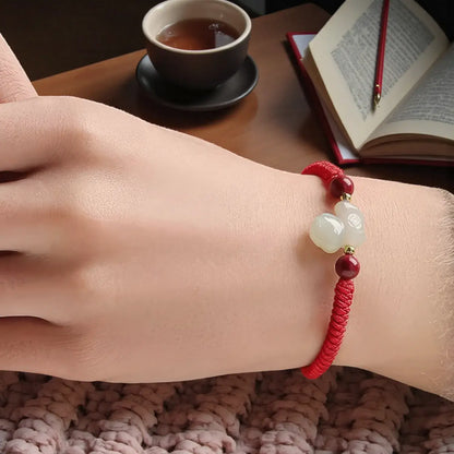 Hand wearing a red string bracelet with a cup of tea and book in the background