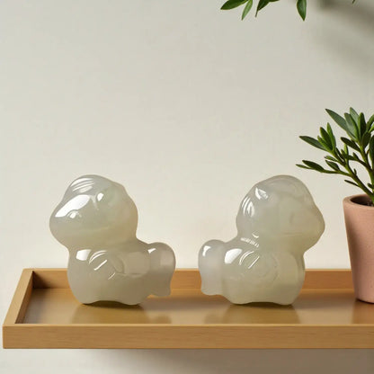 Two white ceramic figures on a wooden tray with a plant in the background