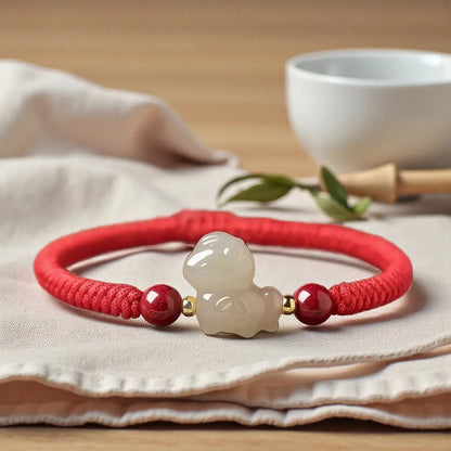 Red bracelet with a white jade charm on a beige cloth with a white bowl in the background