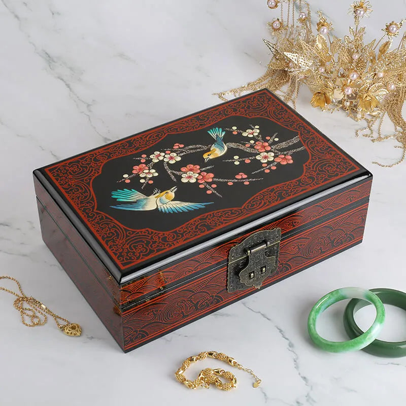 Decorative jewelry box with floral and bird design on a marble surface with jewelry items.