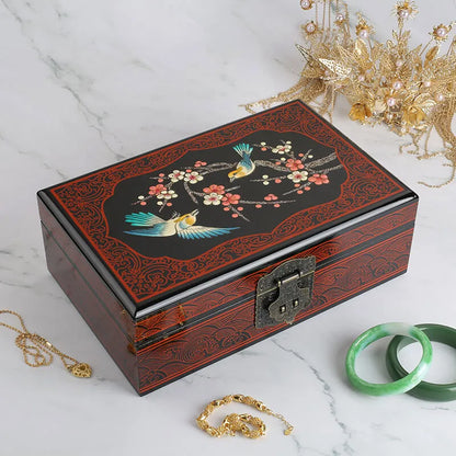 Decorative jewelry box with floral and bird design on a marble surface with jewelry items.