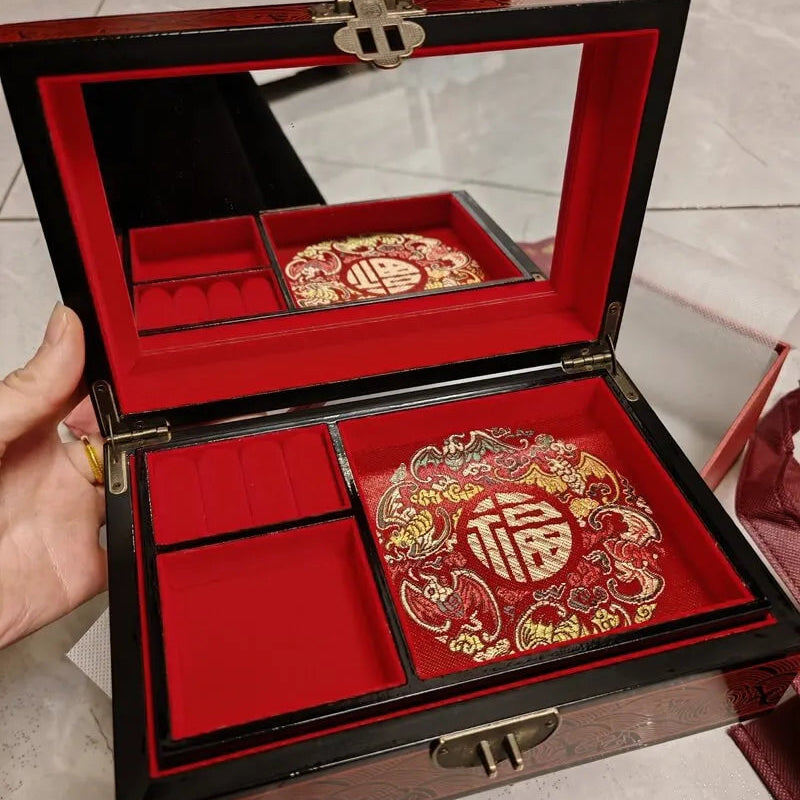 Decorative jewelry box with red and gold interior, held by a hand.