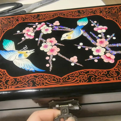 Decorative box with floral and bird design, held open by a hand.