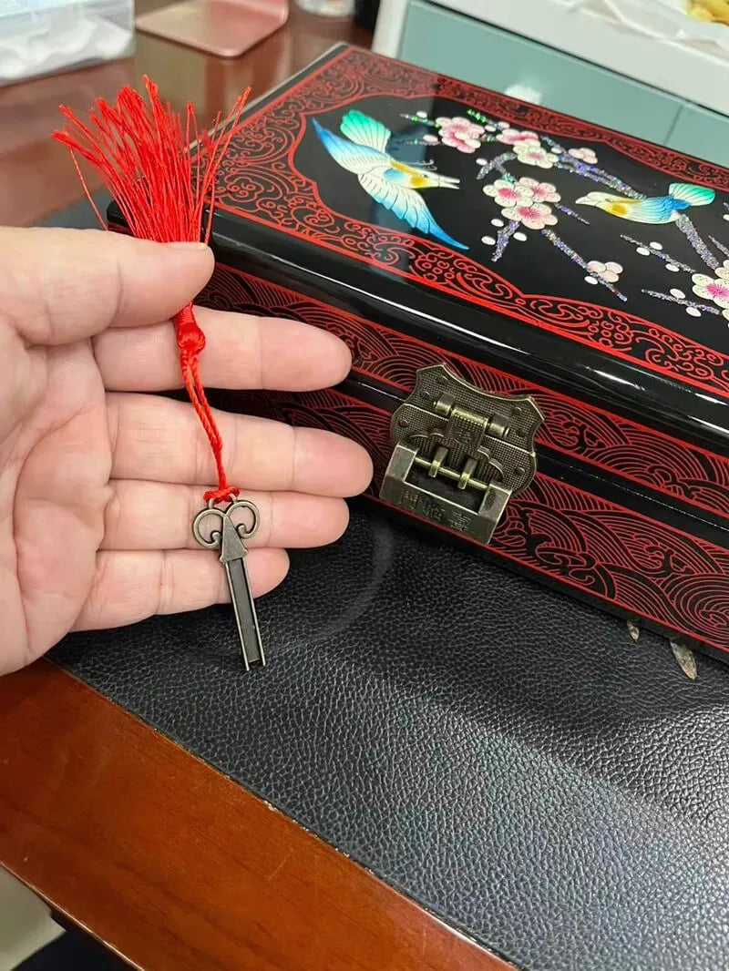 Hand holding a key charm with a red string in front of an embroidered box.