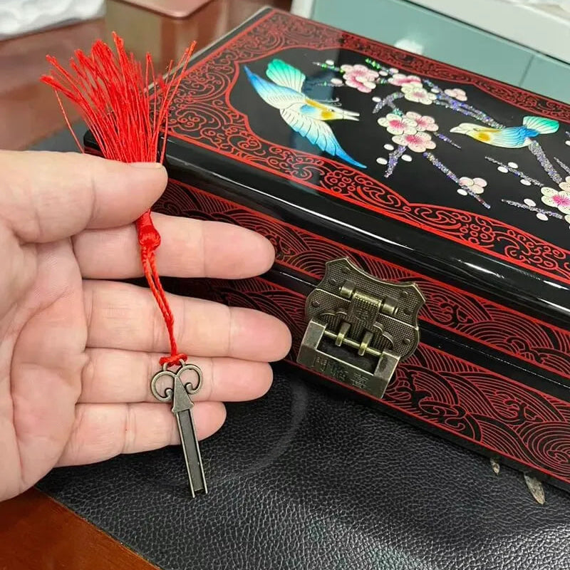 Hand holding a key charm with a red string in front of an embroidered box.