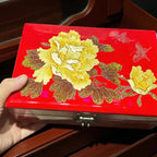 Red jewelry box with yellow floral designs held by a hand.