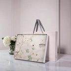 Framed artwork with floral design on a marble surface next to a vase of flowers.