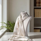 Mannequin wearing a light-colored scarf with floral patterns on a table with a blurred indoor background.