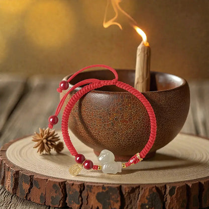 Red beaded bracelet with a charm on a wooden surface with a candle in the background