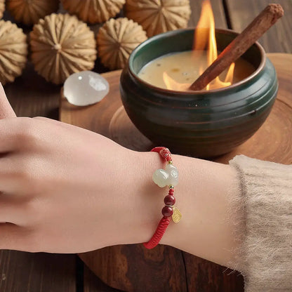 Hand wearing a beaded bracelet with a lit candle and cinnamon stick in the background