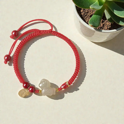Red bracelet with a charm on a light surface next to a small plant