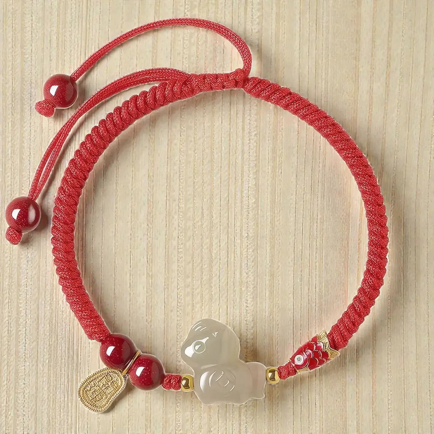 Red string bracelet with decorative beads and charm on a wooden surface