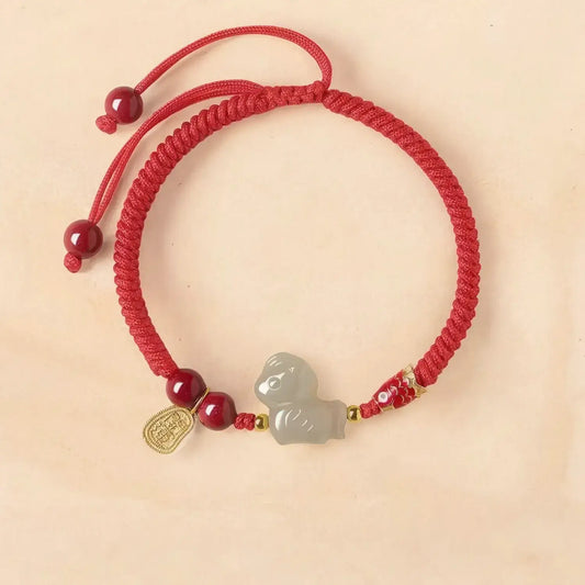Red string bracelet with a gray charm on a beige background