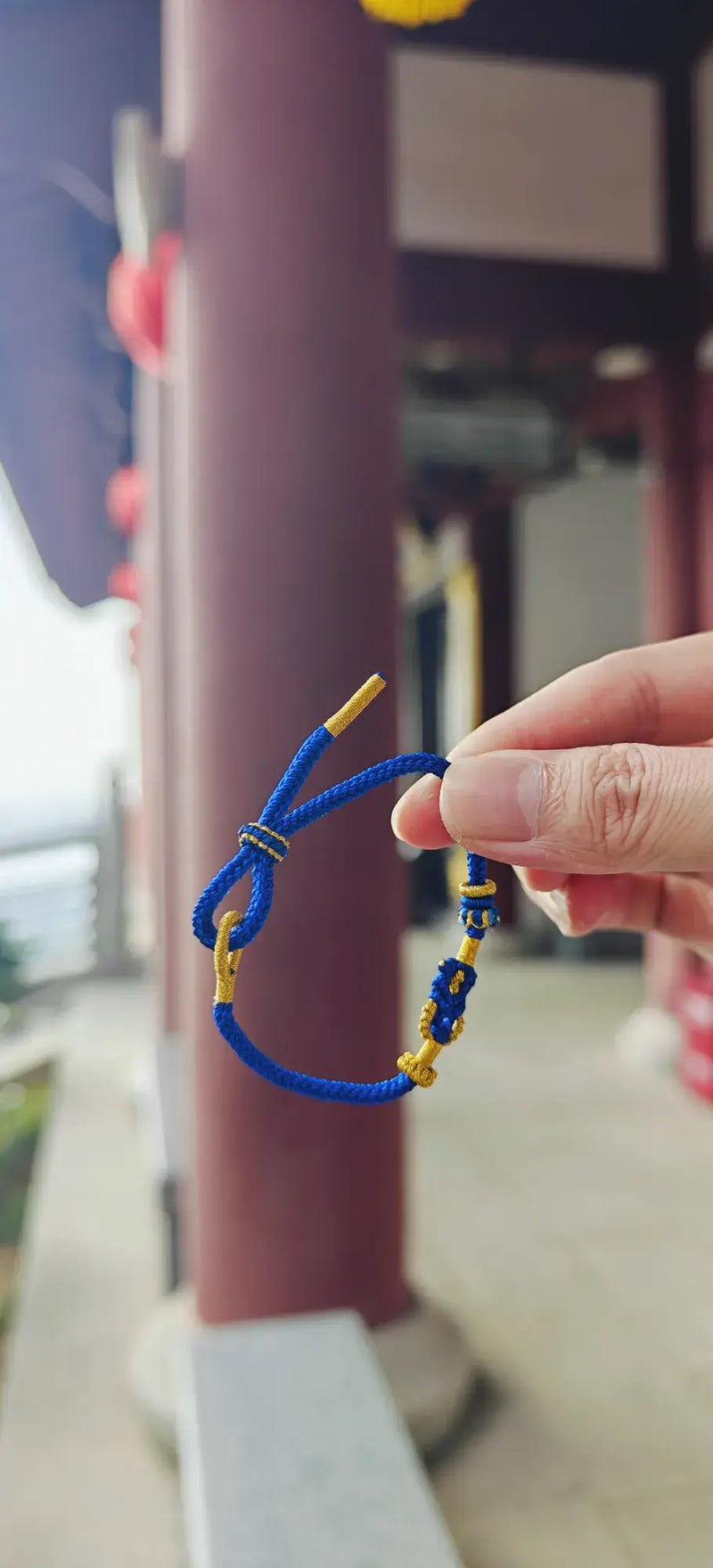Hand holding a blue bracelet with yellow accents against a blurred background