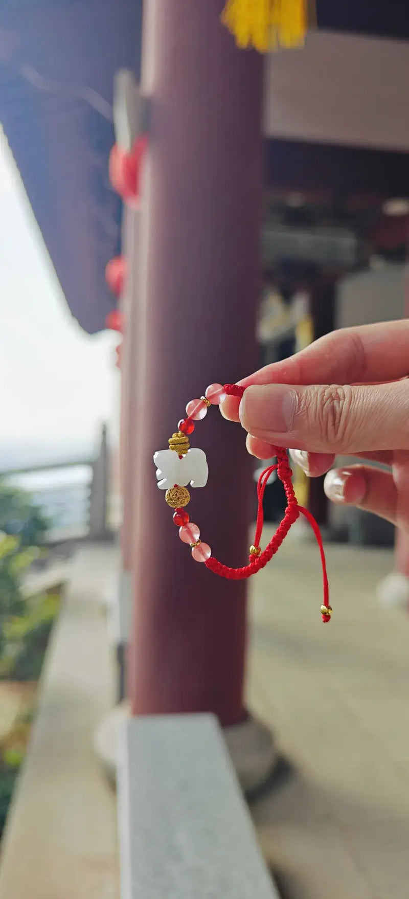 Hand holding a red string bracelet with floral designs against a blurred background