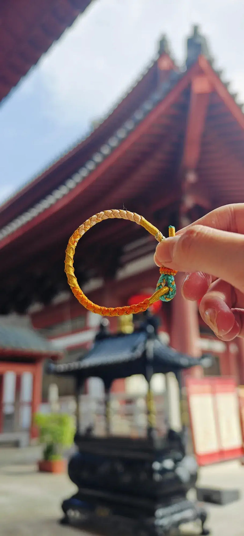 Hand holding a colorful bracelet in front of a traditional Japanese building