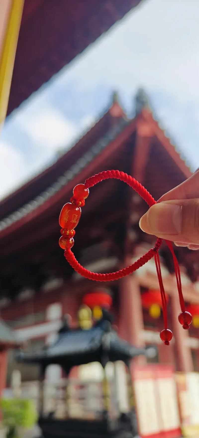 Red beaded bracelet held in front of a traditional Japanese building