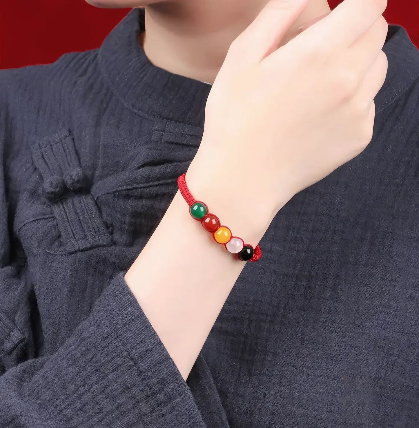 Person wearing a colorful beaded bracelet on a dark blue garment with a red background