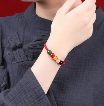 Person wearing a colorful beaded bracelet on a dark blue garment with a red background