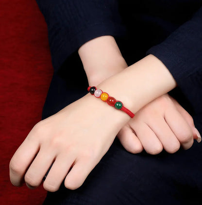 Close-up of a wrist wearing a colorful beaded bracelet against a dark background