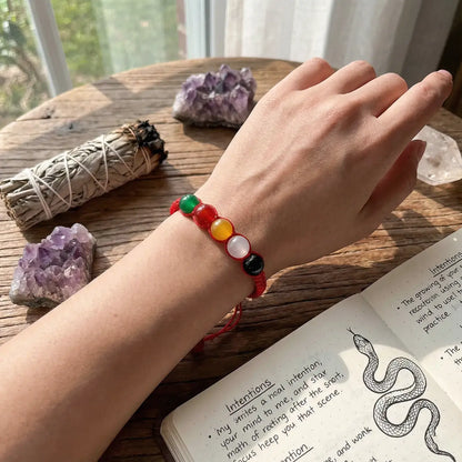 Hand wearing a colorful beaded bracelet on a wooden surface with crystals and a book.