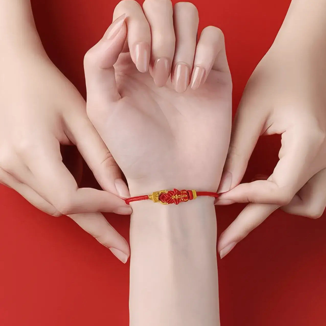 Red bracelet being worn on a wrist with two hands adjusting it against a red background