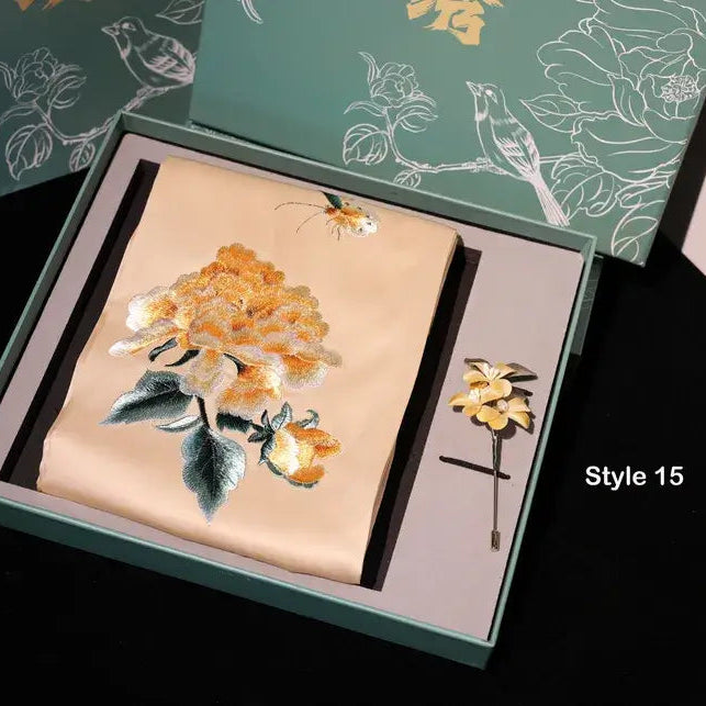 Embroidered floral design on fabric with a matching brooch in a decorative box.