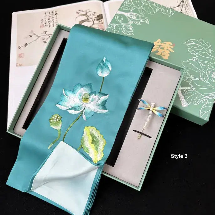 Embroidered lotus design on a turquoise fabric with a pen set in a box.