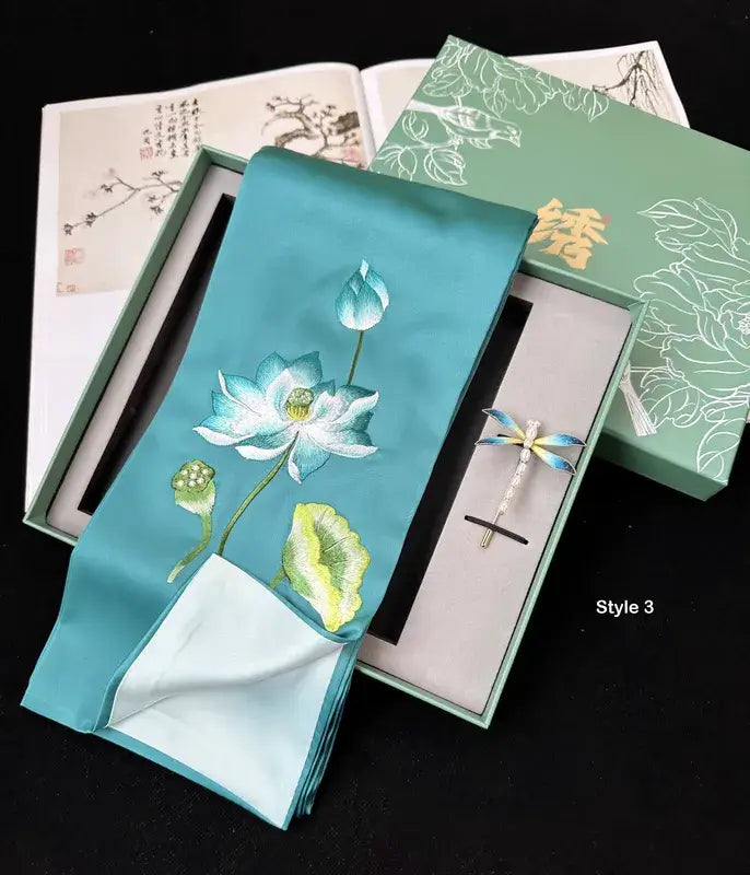 Embroidered lotus design on a turquoise fabric with a pen set in a box.