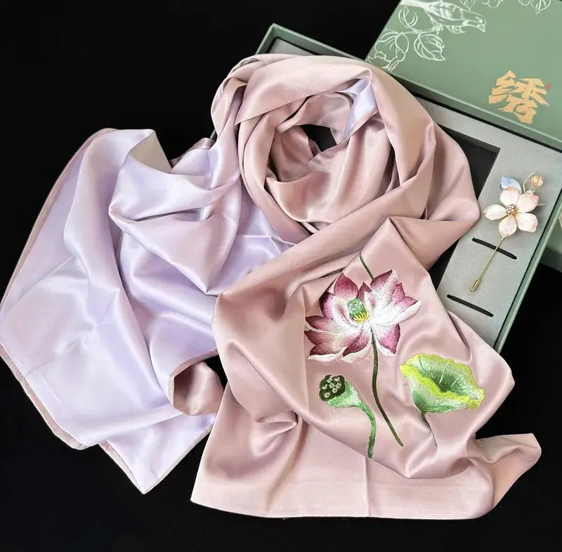 Pink scarf with floral embroidery in front of a green box on a black background
