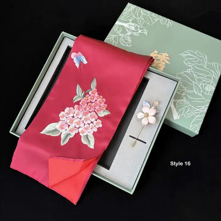 Red fabric with floral embroidery and a brooch in a decorative box on a black background