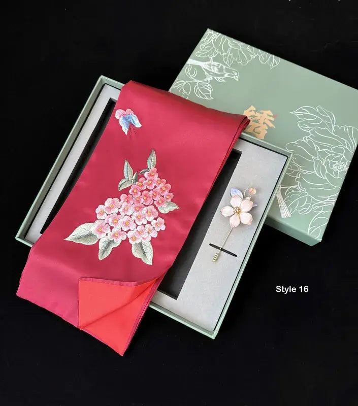 Red fabric with floral embroidery and a brooch in a decorative box on a black background
